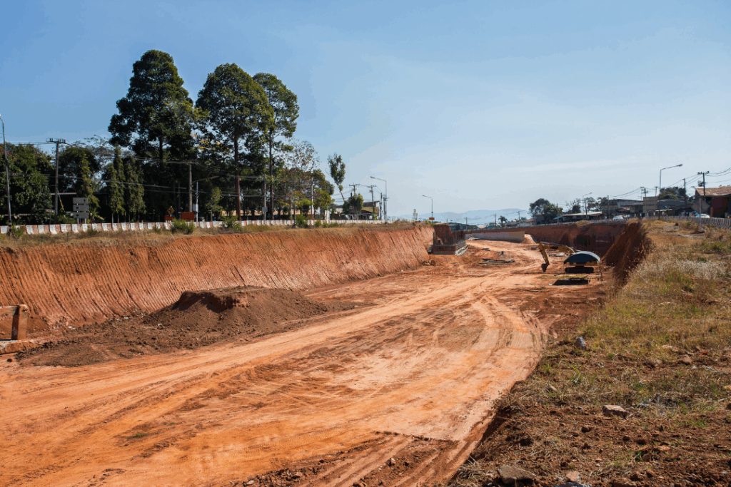 A dirt road with a truck driving along it, surrounded by greenery and open fields.